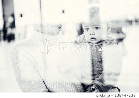 Thoughtful young mother looking trough window holding his infant baby boy child while waiting to board an airplane at airport terminal departure gates. Travel with baby concept Thoughtful young mother looking trough window holding his infant baby boy child while waiting to board an airplane at airport terminal departure gates. Travel with baby concept 139447238