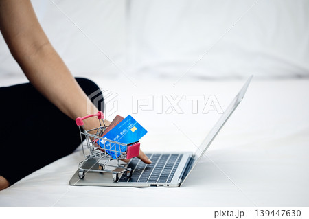 Online shopping concept with laptop, shopping cart and credit cards on bed, representing ecommerce payment, digital banking, cashless lifestyle and modern consumer technology at home 139447630