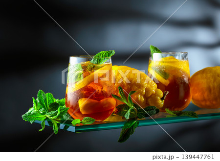 Misted glass of iced tea with fresh lemons and mint branches on a black background. Misted glass of iced tea with fresh lemons and mint branches on a black background. 139447761