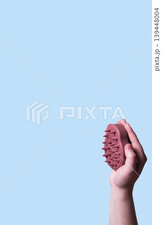 Pink scalp massager brush for hair treatment and care in human hand on blue background. Vertical Pink scalp massager brush for hair treatment and care in human hand on blue background. Vertical 139448004
