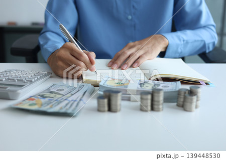 Three stacks of coins arrange separated on the table while businessman writing in a notebook. Financial planning and wealth accumulation for retirement or future investment. Three stacks of coins arrange separated on the table while businessman writing in a notebook. Financial planning and wealth accumulation for retirement or future investment. 139448530