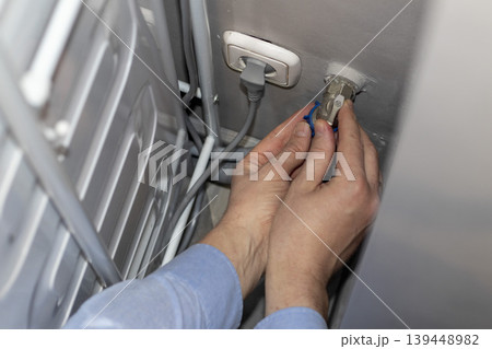 A worker installing or repairing a plumbing valve, likely for a washing machine A worker installing or repairing a plumbing valve, likely for a washing machine 139448982