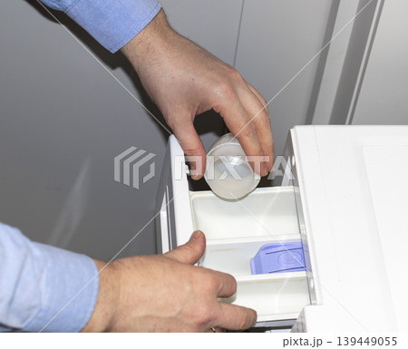 Man opening the detergent dispenser drawer of a front-load washing machine, likely for servicing Man opening the detergent dispenser drawer of a front-load washing machine, likely for servicing 139449055