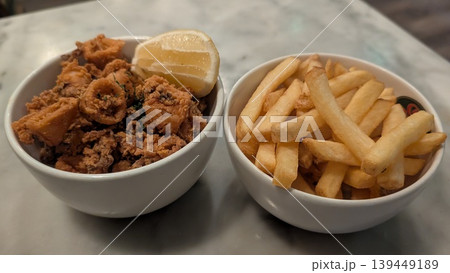 A bowl of french fries and a bowl of crispy fried calamari with cut lemon A bowl of french fries and a bowl of crispy fried calamari with cut lemon 139449189