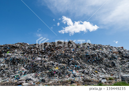 Large mound of trash at city landfill is visible under a clear blue sky with some clouds. Waste includes various types of refuse and debris Large mound of trash at city landfill is visible under a clear blue sky with some clouds. Waste includes various types of refuse and debris 139449235
