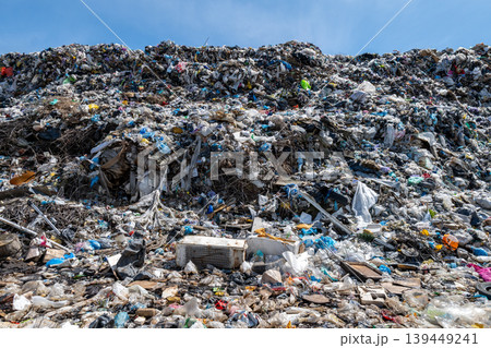 Garbage piles high at a landfill site during daytime with some plastic and debris scattered across the area 139449241