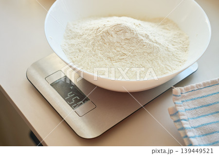 Bowl with flour sits on digital kitchen scale beside towel 139449521