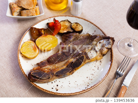Steak churrasco with slices of potato, stewed peppers and aubergine served in a plate with necessary table laying 139453636