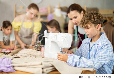 Preteen boy working at machine during group sewing course for kids Preteen boy working at machine during group sewing course for kids 139453686