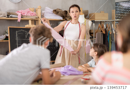 Woman teacher at blackboard conducts theoretical lesson for sewing school children students Woman teacher at blackboard conducts theoretical lesson for sewing school children students 139453717