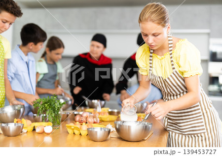 Cooking course - portrait of a girl in an apron who is learning to beat eggs to make pancakes at cooking class 139453727