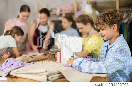 Teen boy child sews during practical lesson at school of young fashion designers Teen boy child sews during practical lesson at school of young fashion designers 139453766