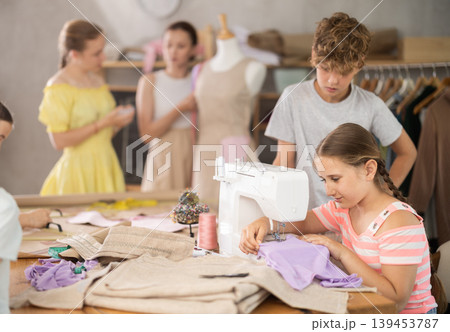 Girl sews on a sewing machine. Boy watches and learns Girl sews on a sewing machine. Boy watches and learns 139453787