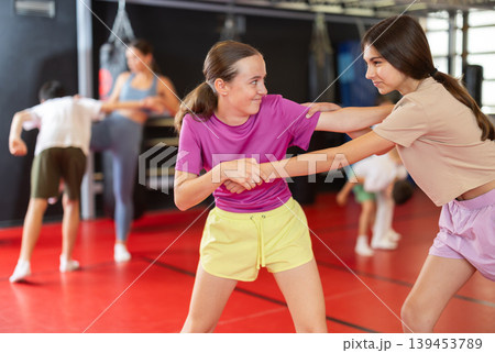 Purposeful engrossed teen girls train during self-defense fight training session in gym Purposeful engrossed teen girls train during self-defense fight training session in gym 139453789