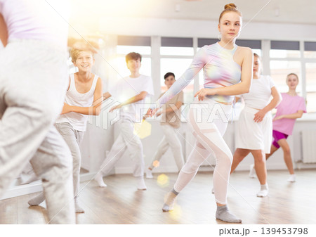 Female girl student repeats movements of unrecognizable teacher during group modern dance class. Female girl student repeats movements of unrecognizable teacher during group modern dance class. 139453798