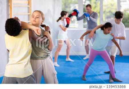 Girls and boys practicing in pair self defence movements with male trainer supervision 139453866