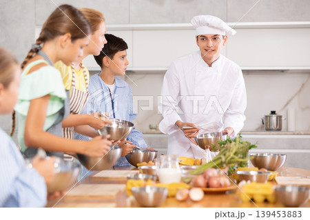 Group of teenagers and friendly chef cook cooking in modern kitchen. Learn to beat raw eggs Group of teenagers and friendly chef cook cooking in modern kitchen. Learn to beat raw eggs 139453883