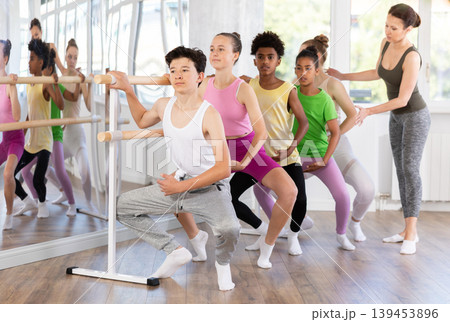 Teenager practicing grand plie at barre at group ballet class Teenager practicing grand plie at barre at group ballet class 139453896