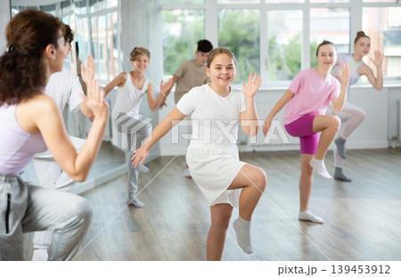 Female teacher performs choreographic exercises and teaches energetic mobile house dance together with teenagers Female teacher performs choreographic exercises and teaches energetic mobile house dance together with teenagers 139453912