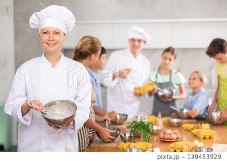 Smiling female chef sharing professional secrets during cooking masterclass for children Smiling female chef sharing professional secrets during cooking masterclass for children 139453929