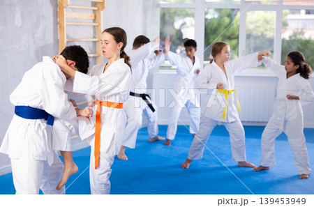 Karate training - girl and boy of different nationalities in pairs exercising karate movements during group training in gym Karate training - girl and boy of different nationalities in pairs exercising karate movements during group training in gym 139453949
