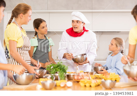 In cooking class, guy cook with bowl in hands tells children participants culinary ticks and tricks 139453981