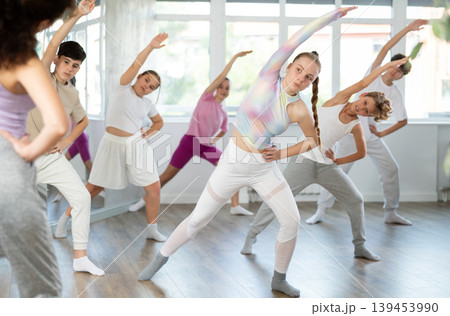 Female girl student repeats movements of unrecognizable teacher during group modern dance class. 139453990