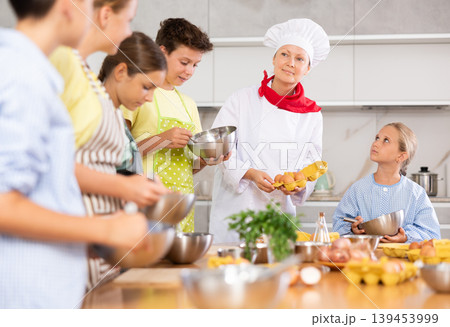 Professional female chef in white uniform conducting culinary class for tweens 139453999