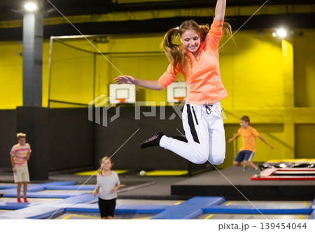 Cheerful teen girl in sport clothes bouncing on trampolines indoors in leisure sport center for kids 139454044