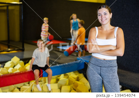 Portrait of cheerful young female in sportswear posing and smiling at camera behind foam cube pit at trampolines center 139454074