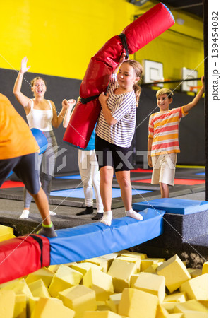 Cheerful school-age boy and girl friends having fun on inflatable gladiator fight arena in indoor amusement center Cheerful school-age boy and girl friends having fun on inflatable gladiator fight arena in indoor amusement center 139454082