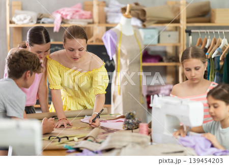 Sewing lesson - a group of teenage children learn to sew on sewing machine and cut fabric 139454203