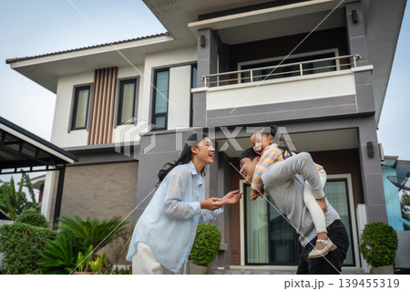 happy family, cheerful child girl piggy back on fatherwith mother while standing in front of their house happy family, cheerful child girl piggy back on fatherwith mother while standing in front of their house 139455319