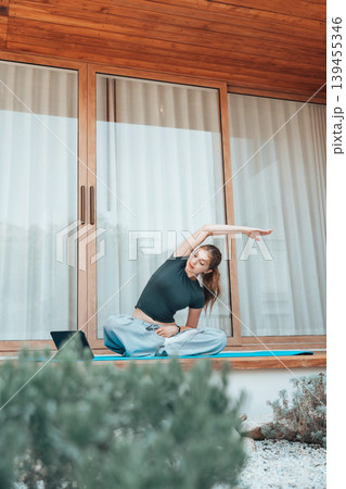 Young woman stretching on a terrace at home while following an online yoga session on a tablet Young woman stretching on a terrace at home while following an online yoga session on a tablet 139455346