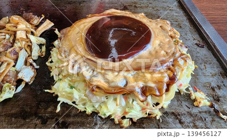 Japanese Okonomiyaki Savory Pancake with Special Sauce and Cabbage on a Hot Griddle 139456127