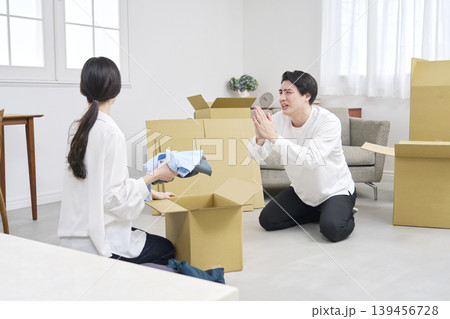 引っ越し中に謝罪する男性と荷造りする女性 引っ越し中に謝罪する男性と荷造りする女性 139456728