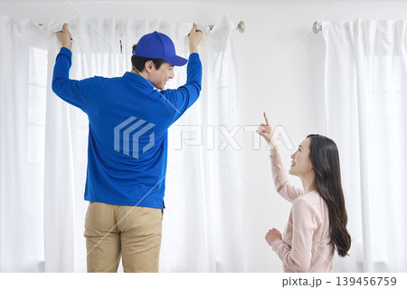 引っ越し業者がカーテンを取り付け女性が指示する 139456759
