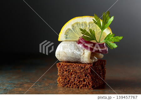 Rye bread canape with herring filet, red onion, lemon, and parsley. 139457767