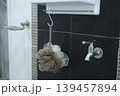 Close-up of a shower loofah hanging on a metal hook against black tile wall. 139457894