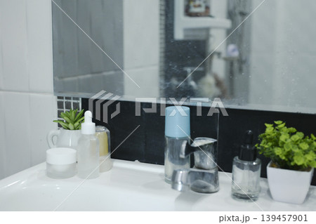 Aesthetic bathroom sink counter with skincare bottles, potted succulents, and clean tiles. 139457901
