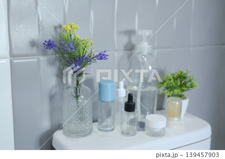 Minimalist bathroom decor with assorted toiletries and floral arrangement against a tiled wall. Minimalist bathroom decor with assorted toiletries and floral arrangement against a tiled wall. 139457903