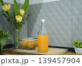 Refreshing cold orange juice bottle and glass with citrus fruits against a grey tile background. 139457904