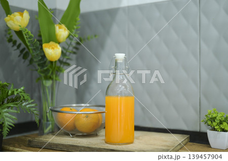 Refreshing cold orange juice bottle and glass with citrus fruits against a grey tile background. Refreshing cold orange juice bottle and glass with citrus fruits against a grey tile background. 139457904