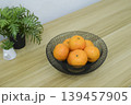 Fresh oranges in a black wire mesh fruit bowl on a wooden table. 139457905