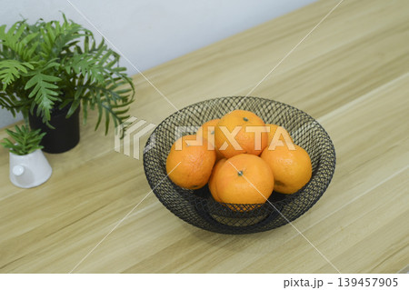 Fresh oranges in a black wire mesh fruit bowl on a wooden table. Fresh oranges in a black wire mesh fruit bowl on a wooden table. 139457905