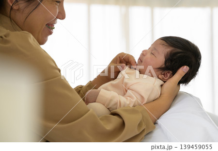 Happy newborn baby girl or boy sleeping on mother arm. Smiling mother touching chin of infant daughter or son on bed at home. Infant Love and new life concept Happy newborn baby girl or boy sleeping on mother arm. Smiling mother touching chin of infant daughter or son on bed at home. Infant Love and new life concept 139459055