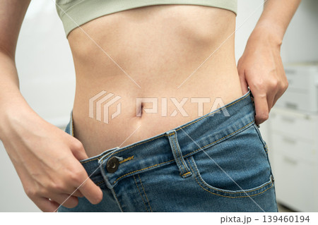Young Asian woman losing weight wearing loose pants in oversize jeans. Young Asian woman losing weight wearing loose pants in oversize jeans. 139460194