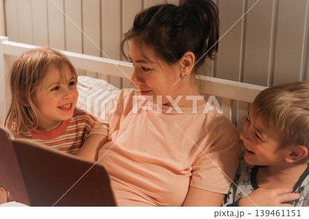 Family bedtime stories. A mother reads a story to her children, wrapped in a blanket. Children listen to soothing stories. A cozy family scene before bed in a softly lit bedroom. Copy space. Banner 139461151