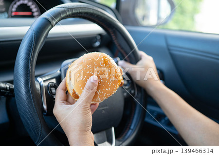 Asian woman driver hold ice coffee cup and sandwich bread for eat and drink in car, dangerous and risk an accident. Asian woman driver hold ice coffee cup and sandwich bread for eat and drink in car, dangerous and risk an accident. 139466314