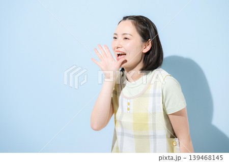 水色背景で保育士や介護士、主婦として働く、応援や口コミなどの笑顔のエプロンを付けた女性の横顔 139468145